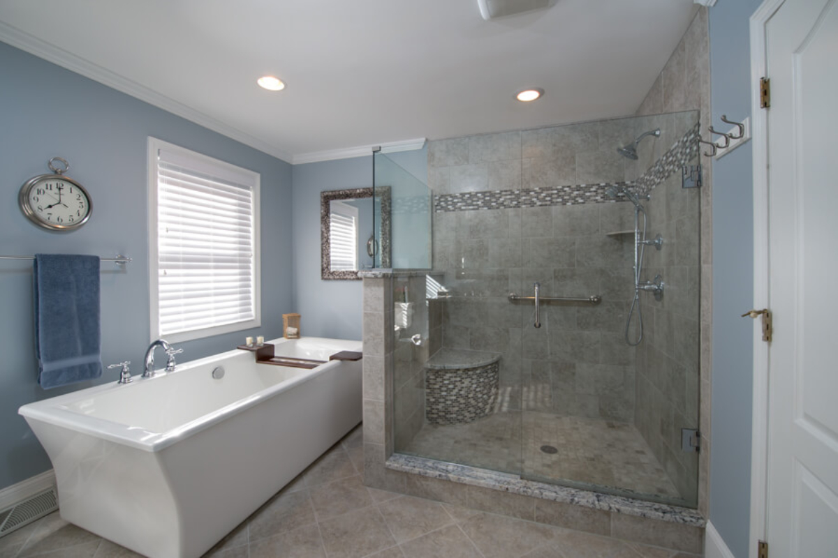 Large shower with gray tiling and corner seat.