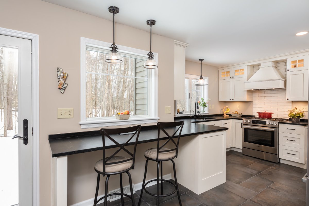 Black bar top in kitchen with white cabinets and dark tile floor.